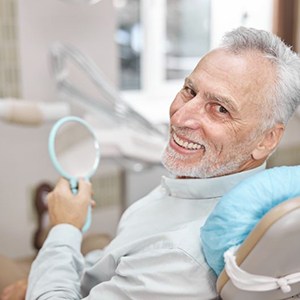 Happy dental patient holding mirror, looking over his shoulder