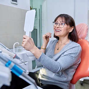 Dental patient holding mirror, admiring her new teeth