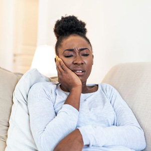 Woman sitting on her sofa, suffering from toothache pain