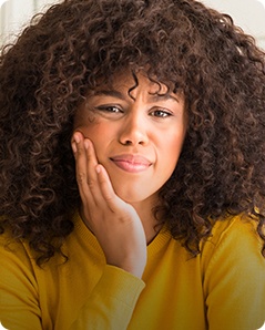 Woman in yellow blouse holding side of her face in pain