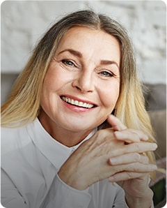 Older woman smiling in front of white brick wall