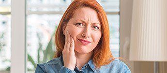 red haired woman holding jaw in severe pain