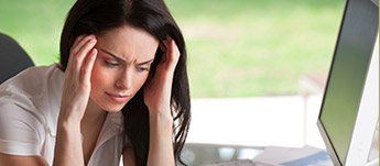 woman holding head in front of computer