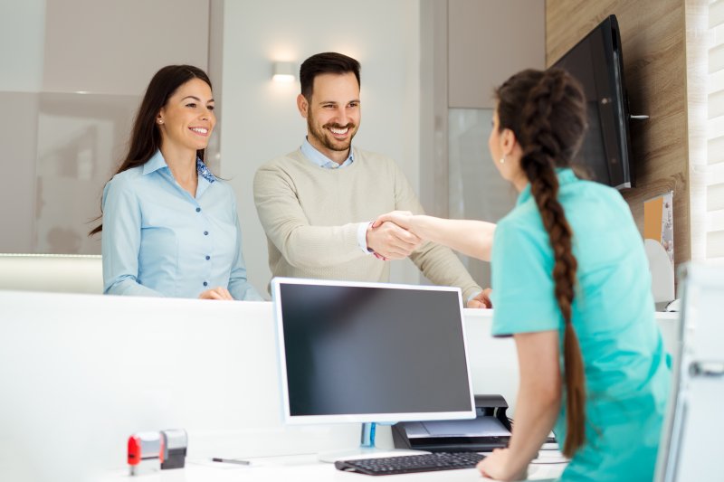 a couple shaking hands with a dental receptionist