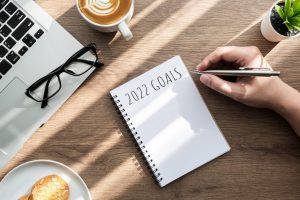 Person writing New Year’s resolutions for 2022 in notebook