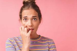 Portrait of woman biting her nails against pink background