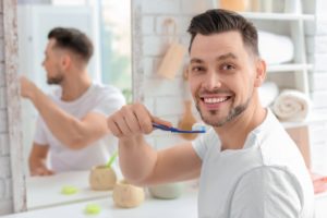 Smiling man brushing his teeth to maintain healthy gums