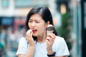 Woman eating ice cream, in pain because of sensitive teeth