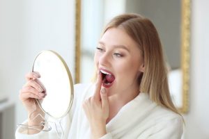 Woman holding mirror, inspecting her teeth