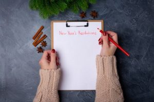 Woman’s hand writing New Year’s resolutions on clipboard