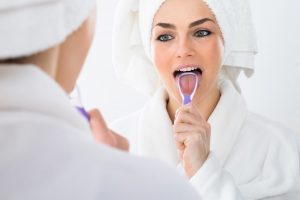 attractive woman using tongue scraper in front of mirror