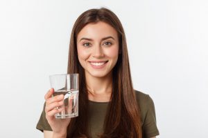 smiling young woman drinking water to benefit her dental health