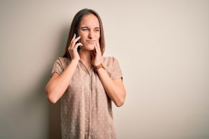 woman in beige blouse with toothache calling emergency dentist