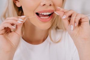 woman in white shirt flossing between front teeth